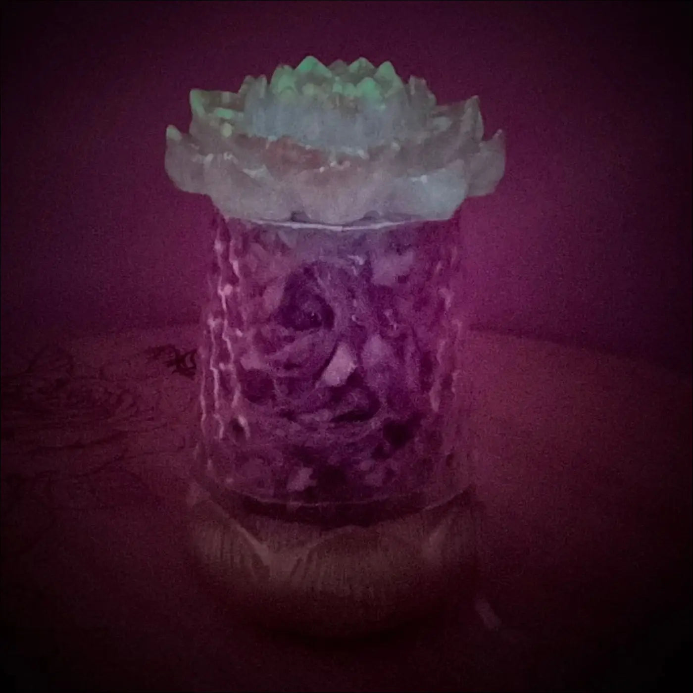 A translucent textured glass candle holder with a frosted green lotus flower lid in a multi-colored app controlled light