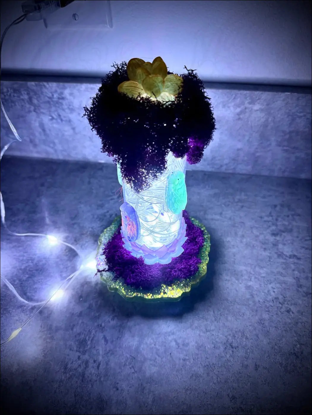 A glowing resin cicadas lamp with a white usb, textured black and purple moss top, and golden lotus petals