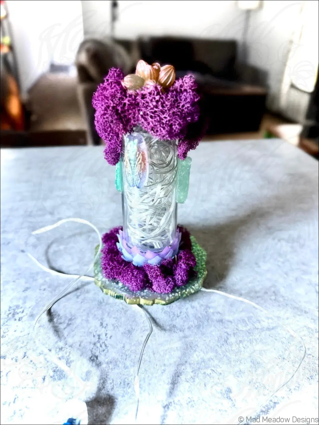 A clear glass bottle with vibrant purple moss and green resin accents featuring resin cicadas and a white usb light