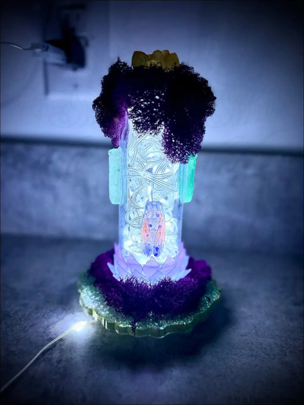 A glowing resin cicadas lamp with intricate etching on a purple and green base using a white usb light