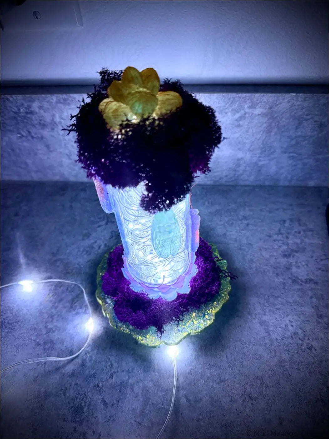 A glowing white usb resin cicadas lamp in a vintage glass bottle with etched patterns and purple moss accents