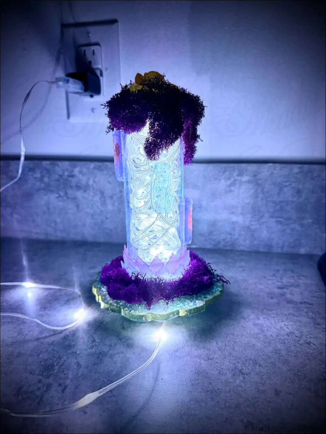 A glowing translucent resin cicadas lantern with white usb light featuring intricate etched designs and purple mossy top