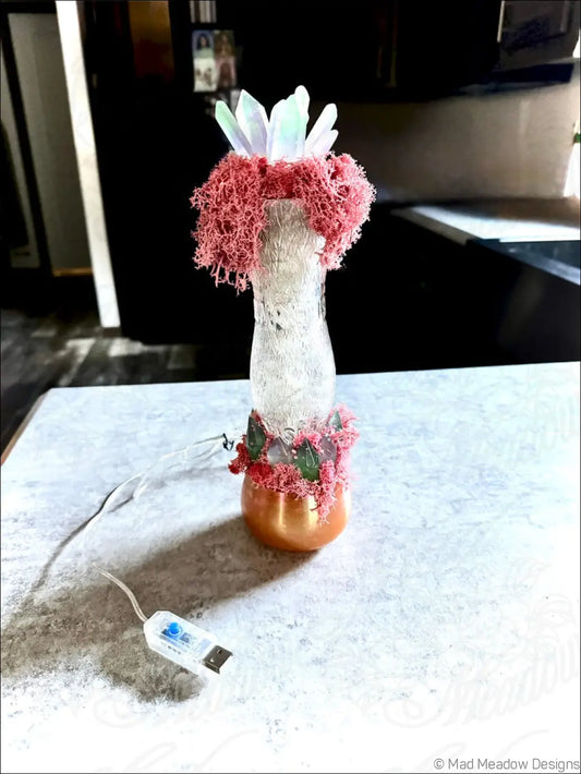 A translucent glass vase with a copper base and pink moss accents in a 1920s hourglass whistle vintage style bottle design