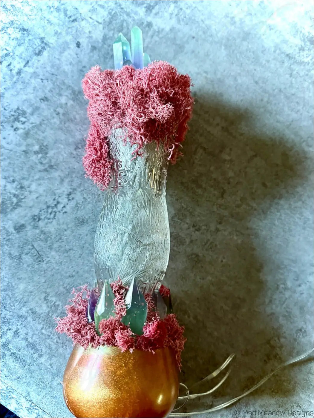 A translucent glass vase with frosted texture and gold base holding pink moss and resin crystals in a whistle soda vintage style