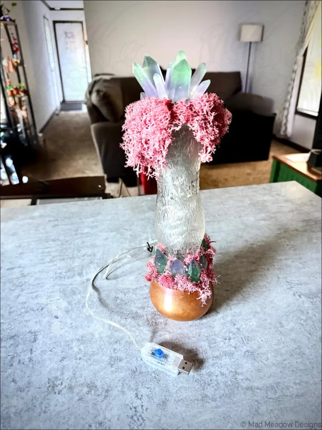 A glowing translucent glass lamp with pink moss green crystals in a whistle soda vintage 1920s hourglass whistle bottle