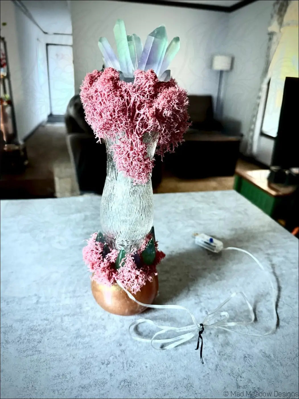 A clear textured glass vase with a copper base and pink moss accents in a 1920s hourglass whistle vintage bottle design