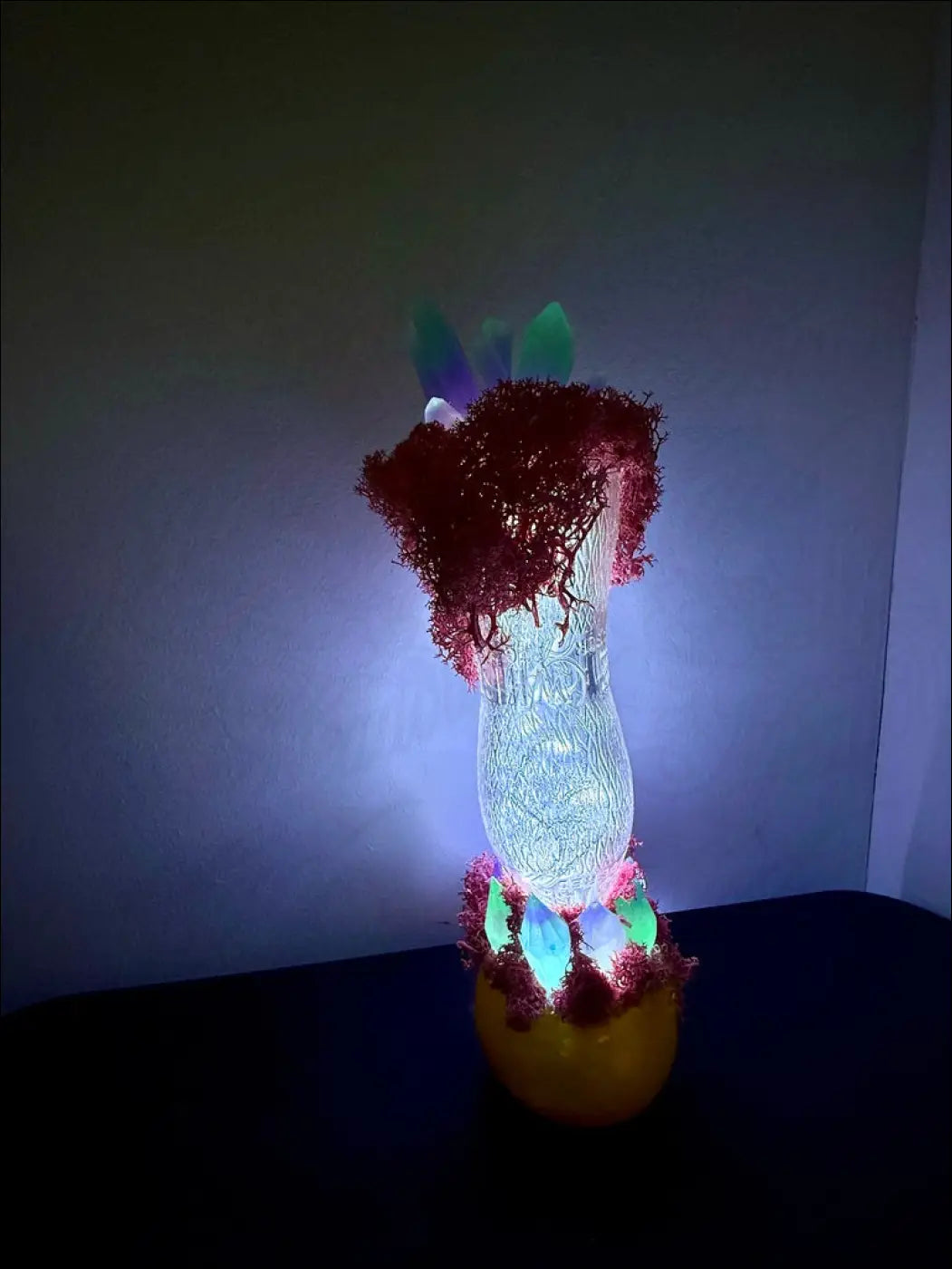 A glowing translucent glass vase with textured surface and red moss around the neck in a 1920s hourglass whistle bottle design
