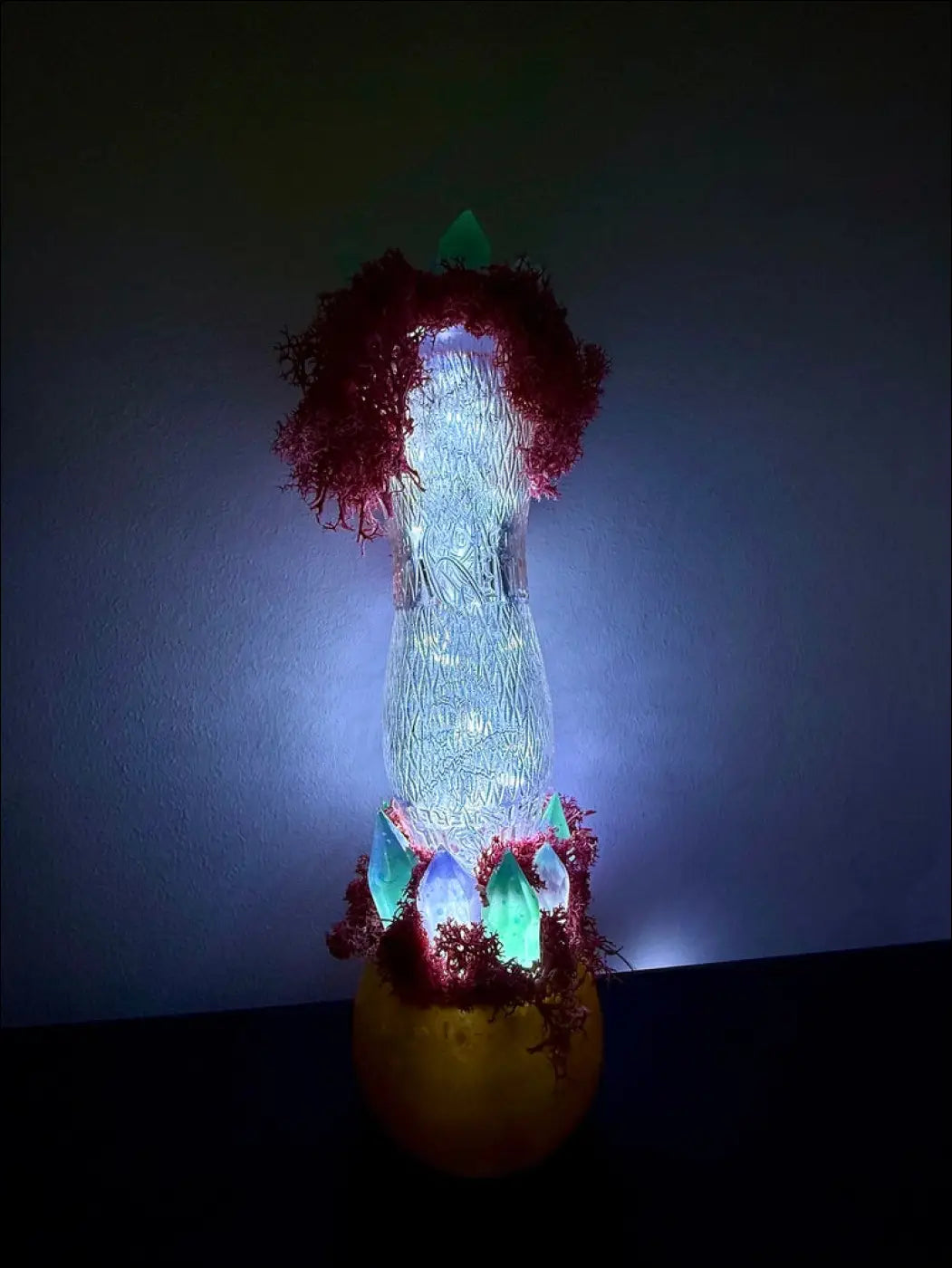 A glowing translucent glass bottle lamp with red tinsel and green crystals inspired by 1920s hourglass whistle soda