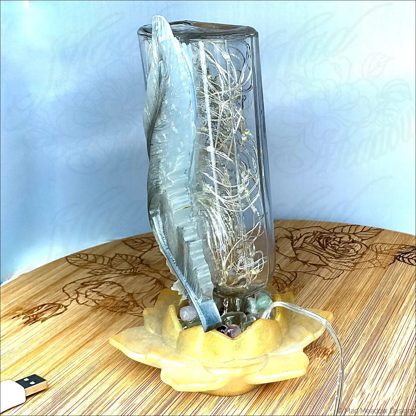 A translucent antique glass apothecary bottle with a silver feather design on a yellow lotus flower base usb light