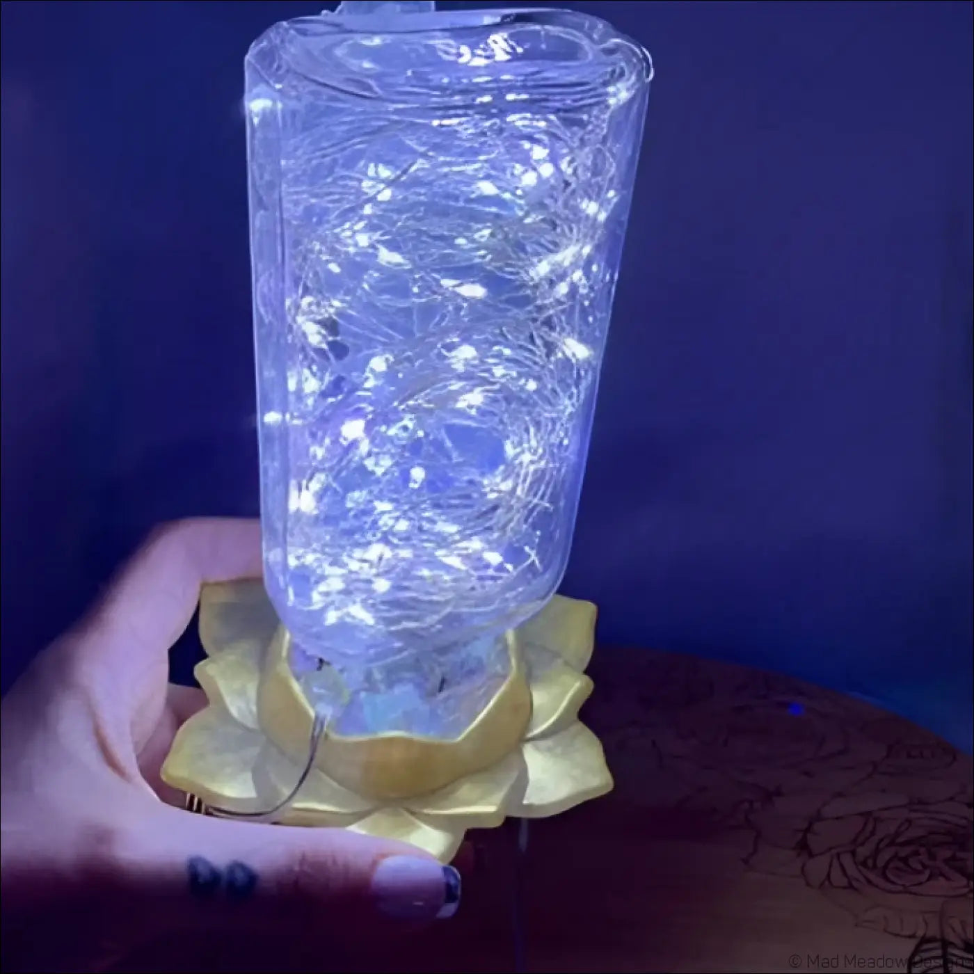 A clear antique glass apothecary bottle lantern with white fairy lights resting on a golden lotus flower base usb light