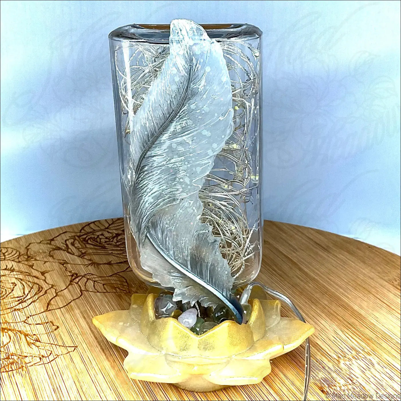 Silver feather sculpture inside a clear glass apothecary bottle resting on a yellow lotus base usb light