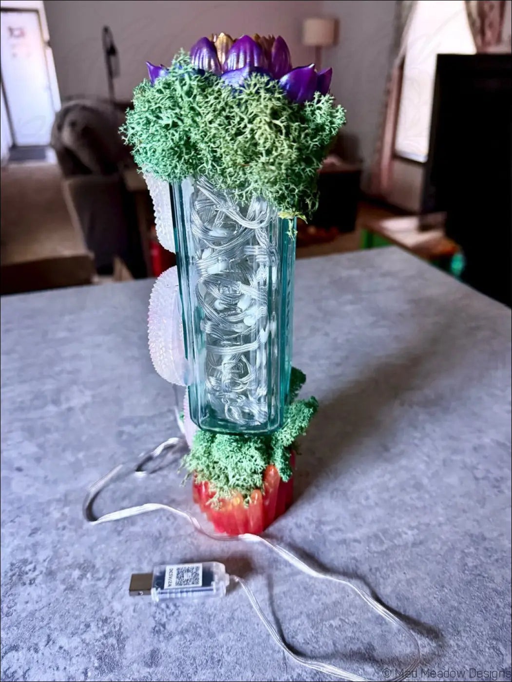 A teal antique glass apothecary bottle usb light with textured surface holds purple artificial flowers moss and crystals