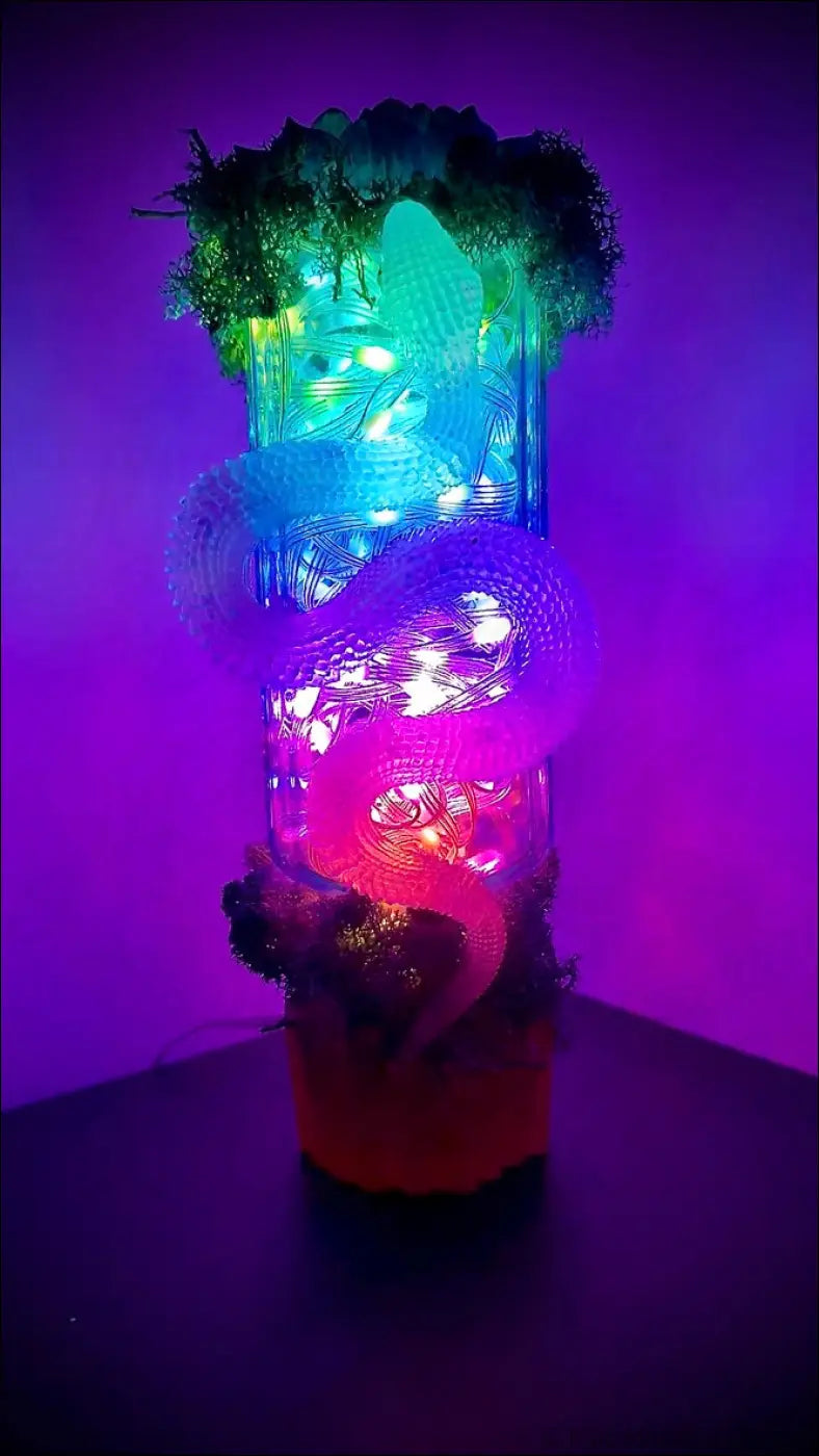 A glowing translucent glass lantern with a dragon design and blue pink led lights on an antique glass apothecary bottle