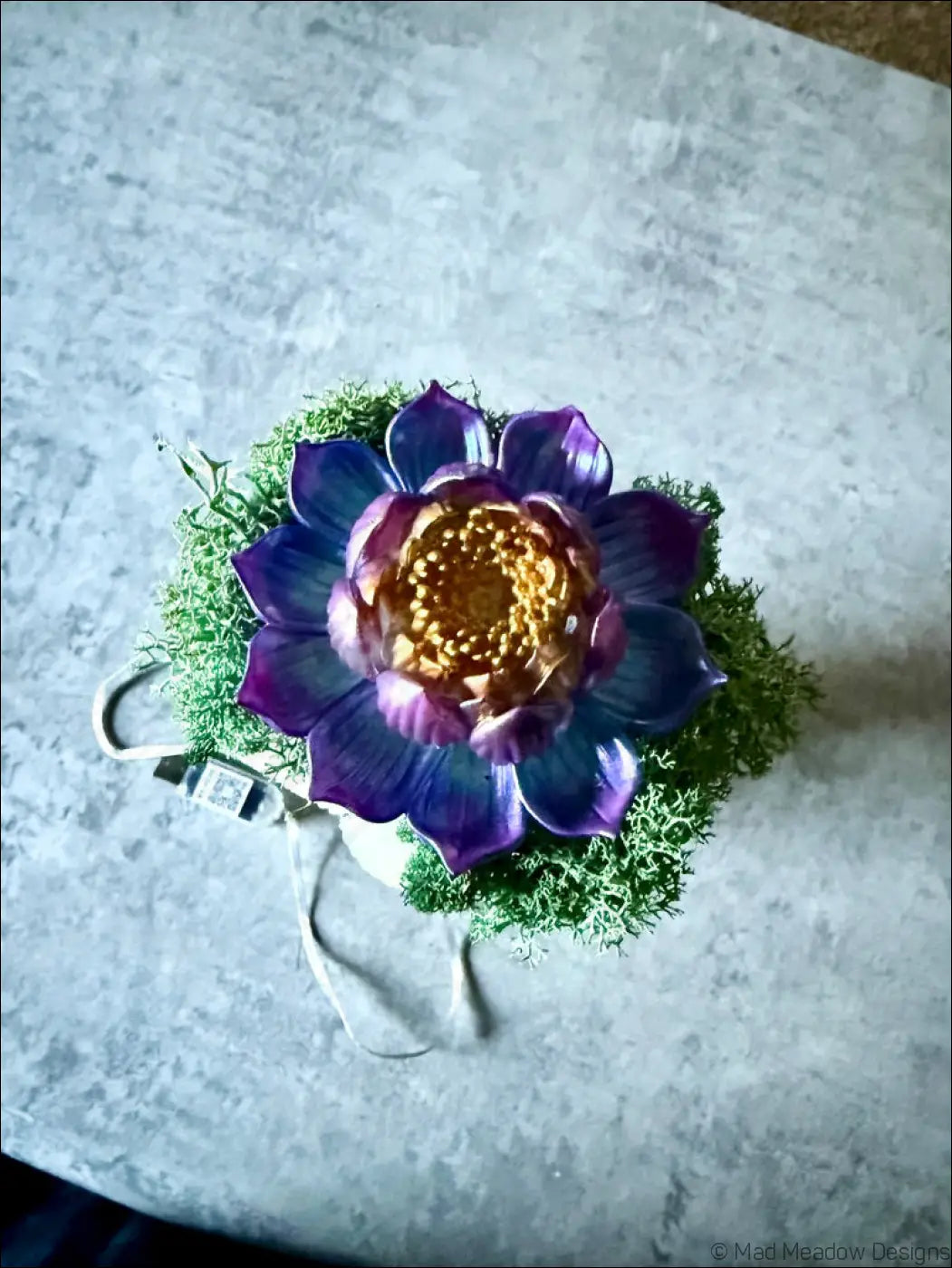 A vibrant purple and gold ceramic lotus flower ornament on an antique glass apothecary bottle usb light with moss and crystals
