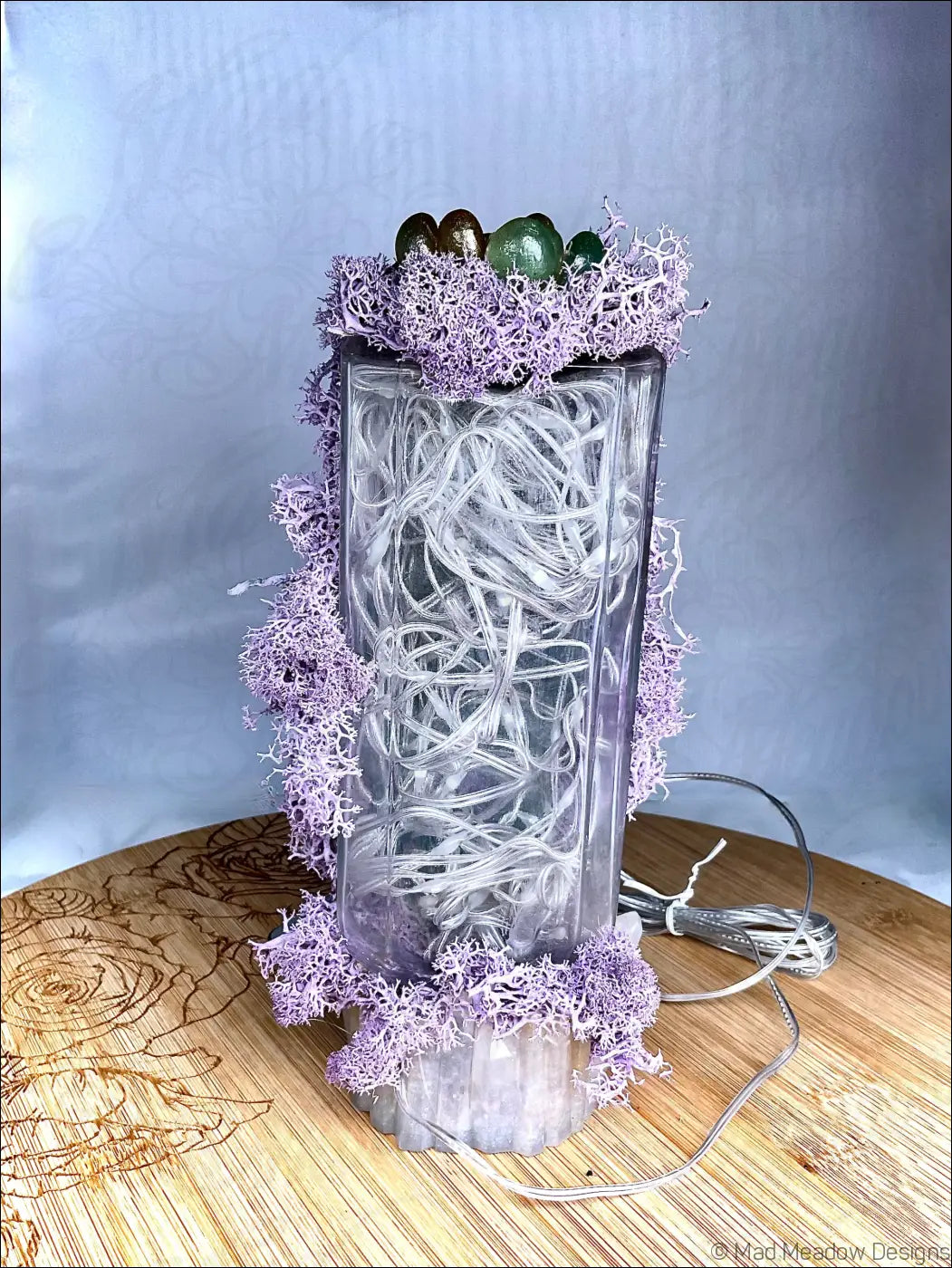 A clear glass apothecary bottle usb light with pastel purple moss white string lights and green gold eggs on top