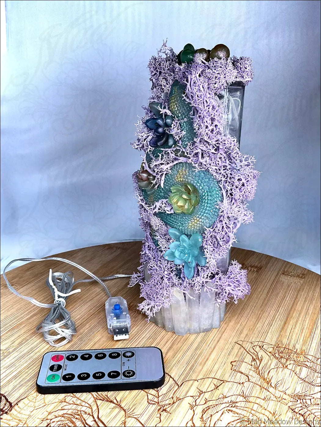 A tall apothecary bottle usb lamp with pastel purple moss, teal succulents, and metallic accents on clear glass base