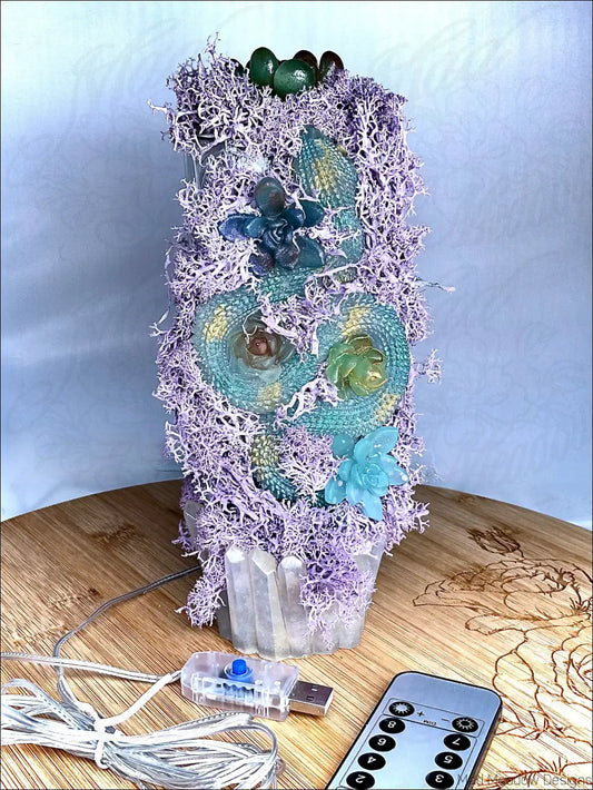 A skull-shaped usb lamp with pastel purple moss, teal resin, succulents, quartz crystals on antique glass bottle