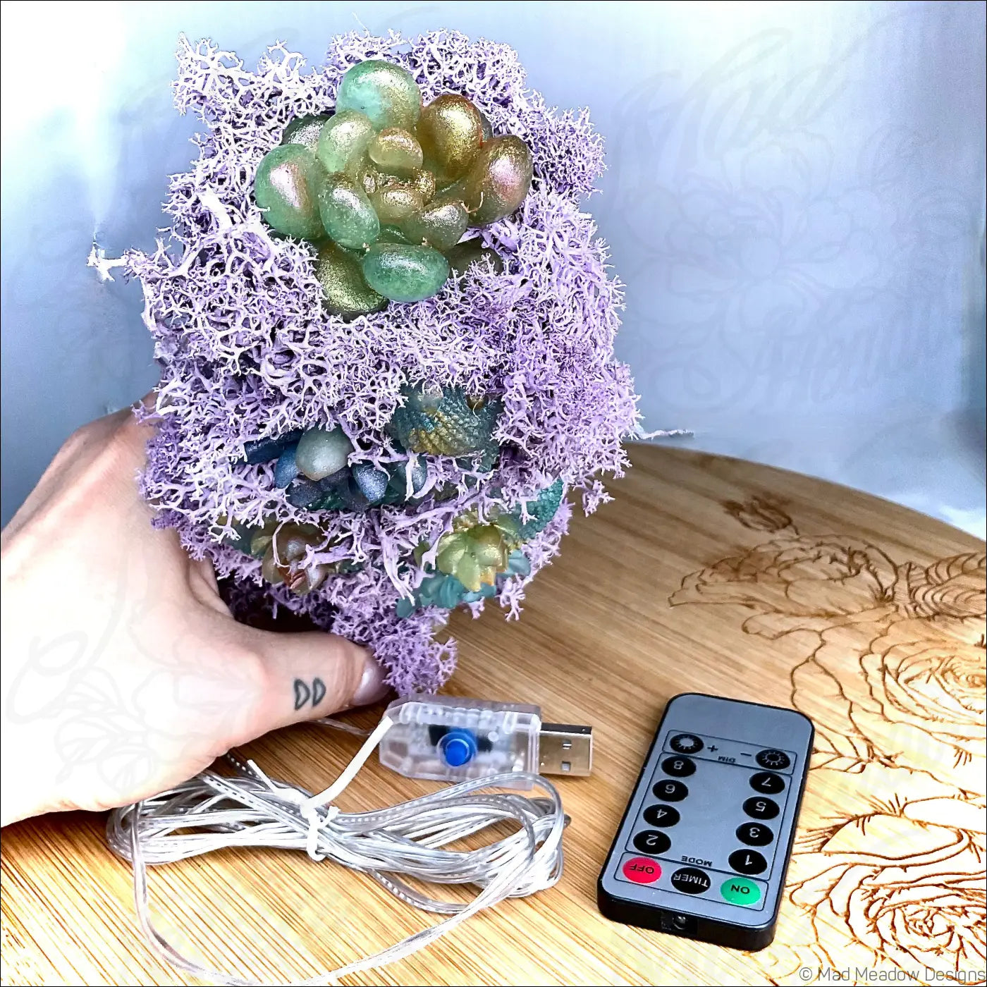 A decorative lamp with green and gold glass beads nestled in pastel purple moss on an antique glass bottle with usb light