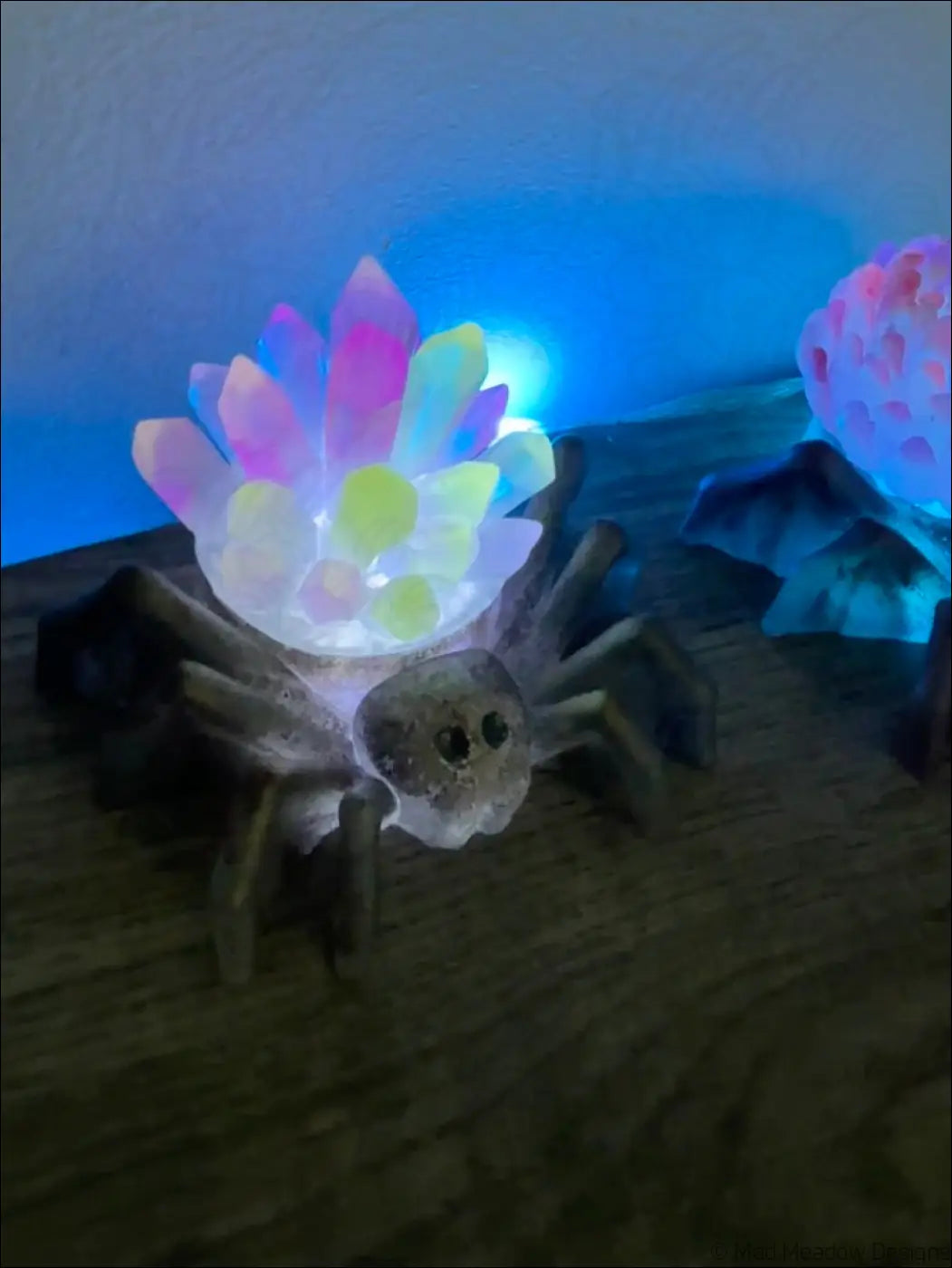 A glowing translucent spider shaped usb led light with a colorful crystalline flower on its back