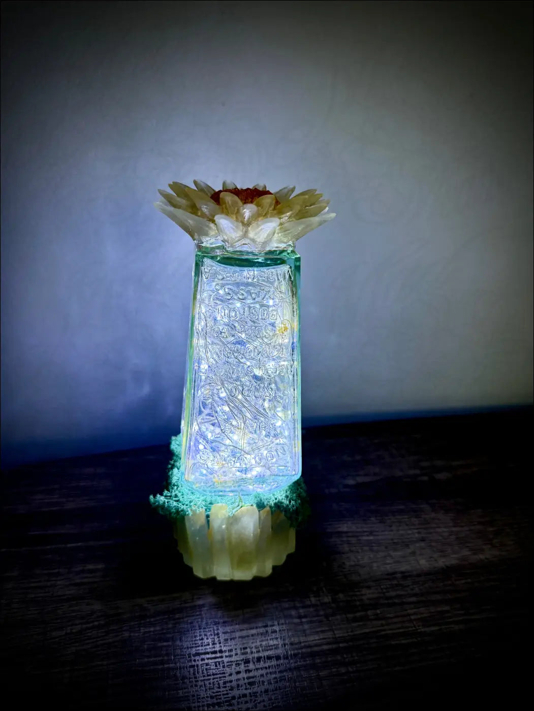 A translucent green glass hair petrole bottle with etched patterns topped with white and yellow flower arrangement