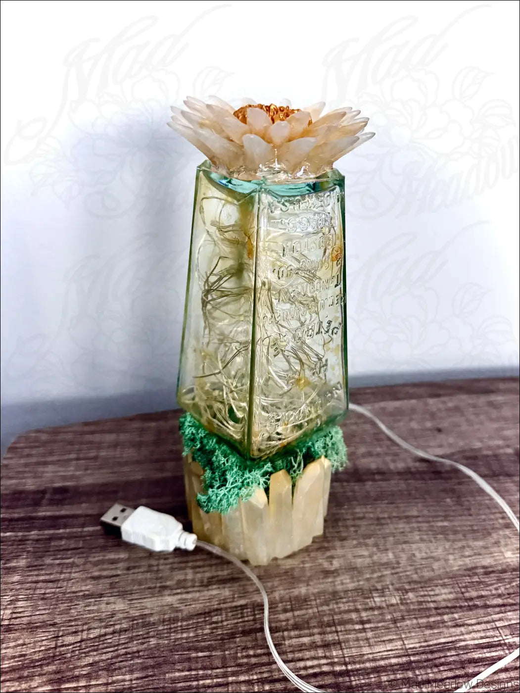 A translucent green glass hair petrole bottle vase with engraved text glowing fairy lights and cream dried flower top