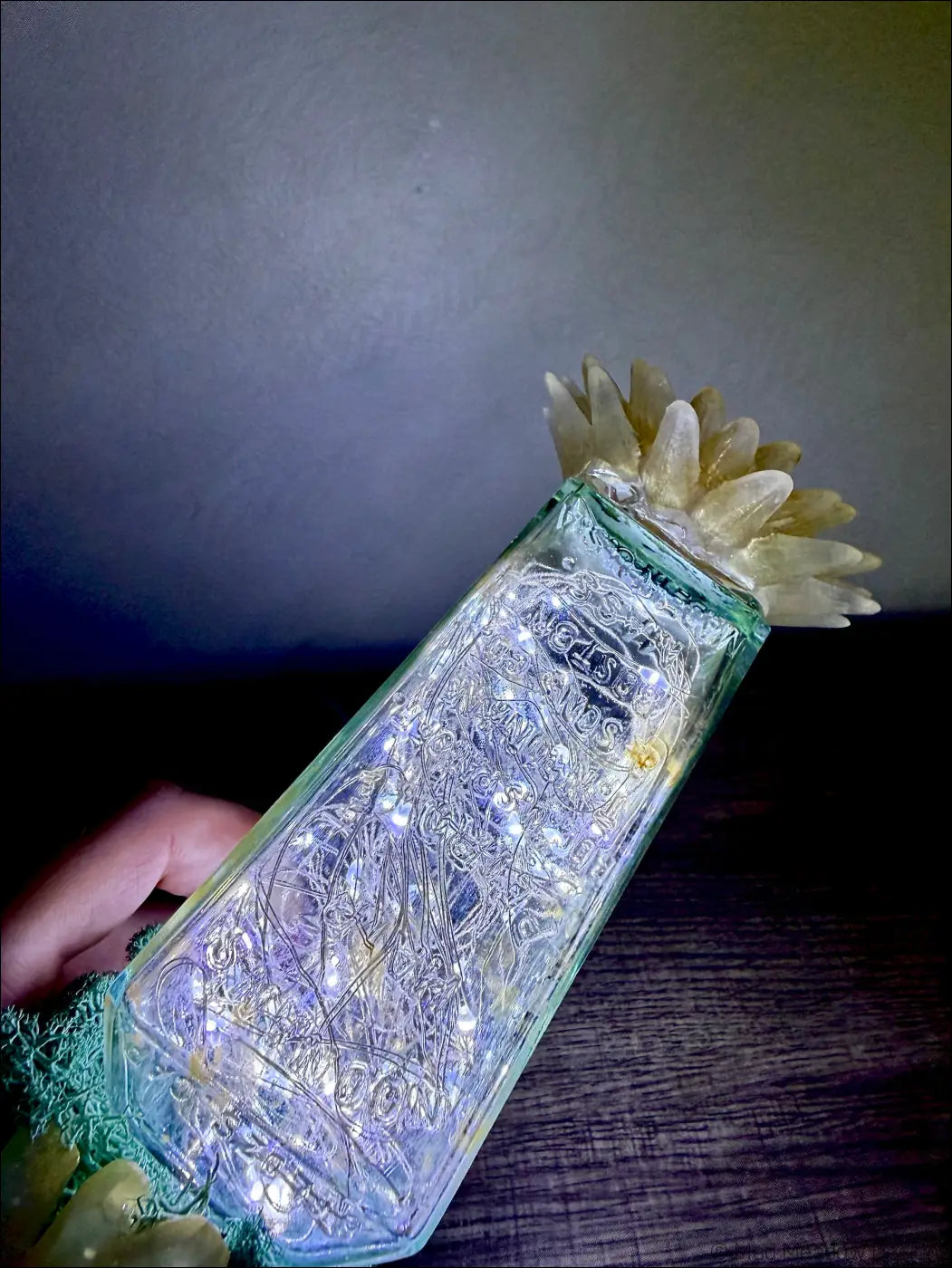 A translucent green glass hair petrole bottle decorated with white crystals and glowing fairy lights inside