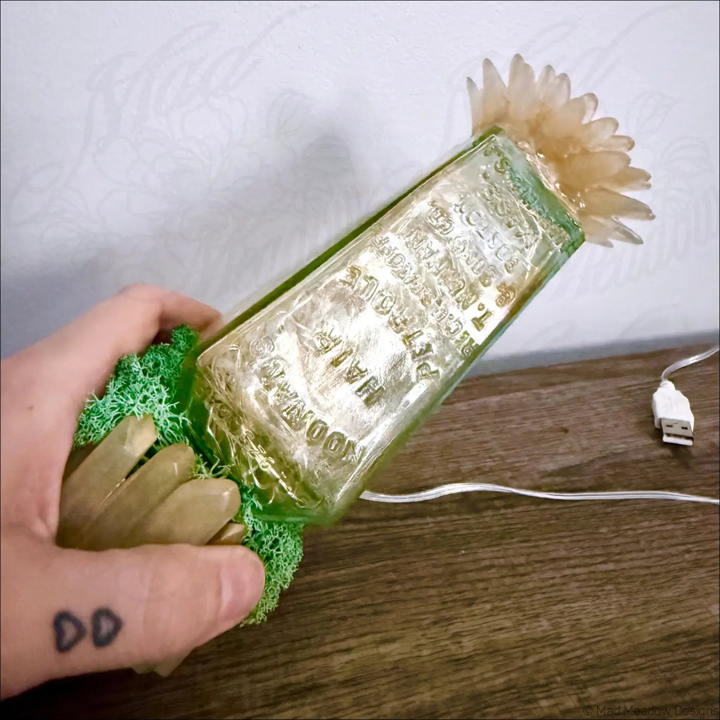 A translucent green hair petrole bottle lamp decorated with beige flowers moss and crystals for usb lighting