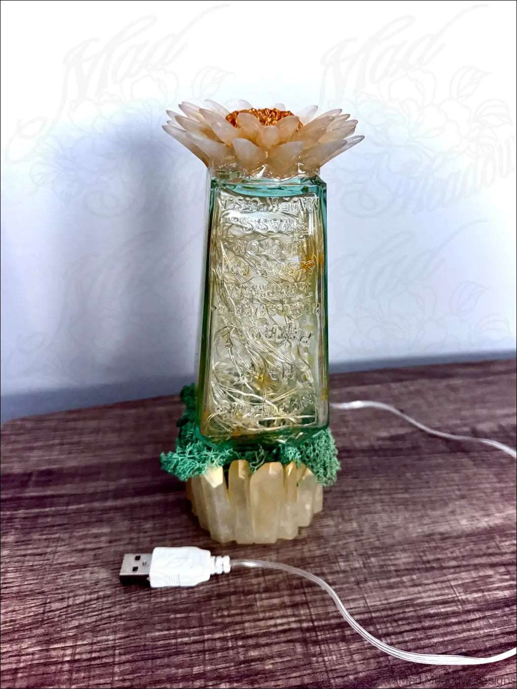 A translucent green glass hair petrole bottle lamp with etched designs topped by a cream flower with moss base