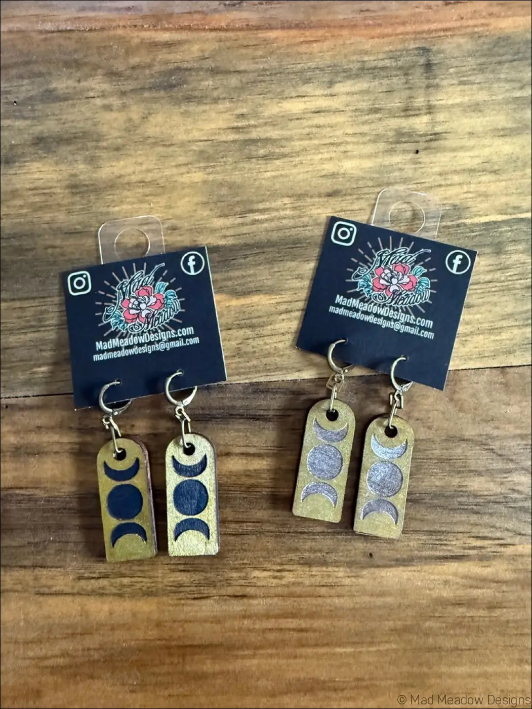 A pair of brass-colored wooden earrings with triple moon hand-painted design in dark blue and silver moon phases