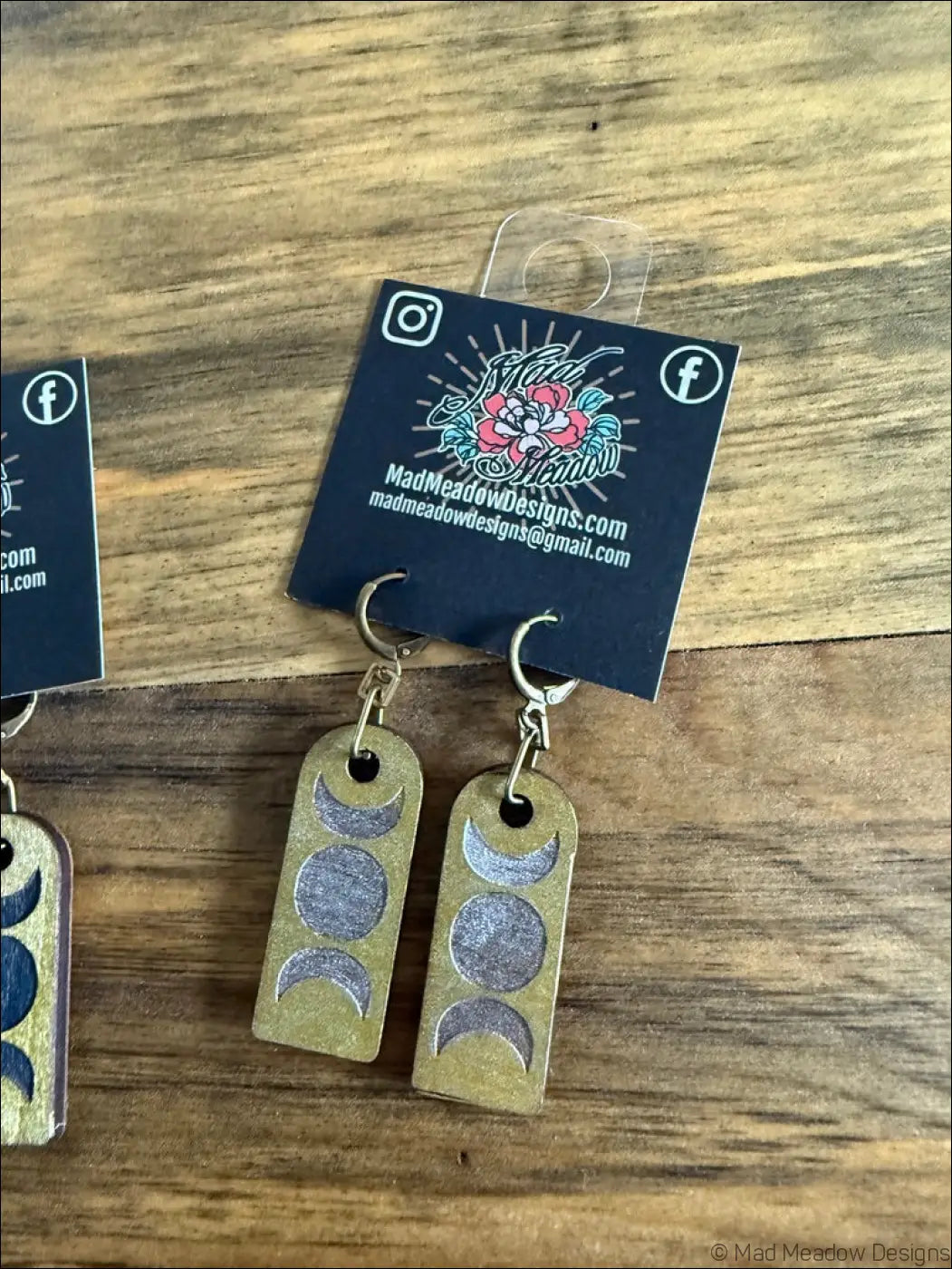 Gold-toned wooden earrings with triple moon design featuring three embossed crescent moons in gray and silver shades