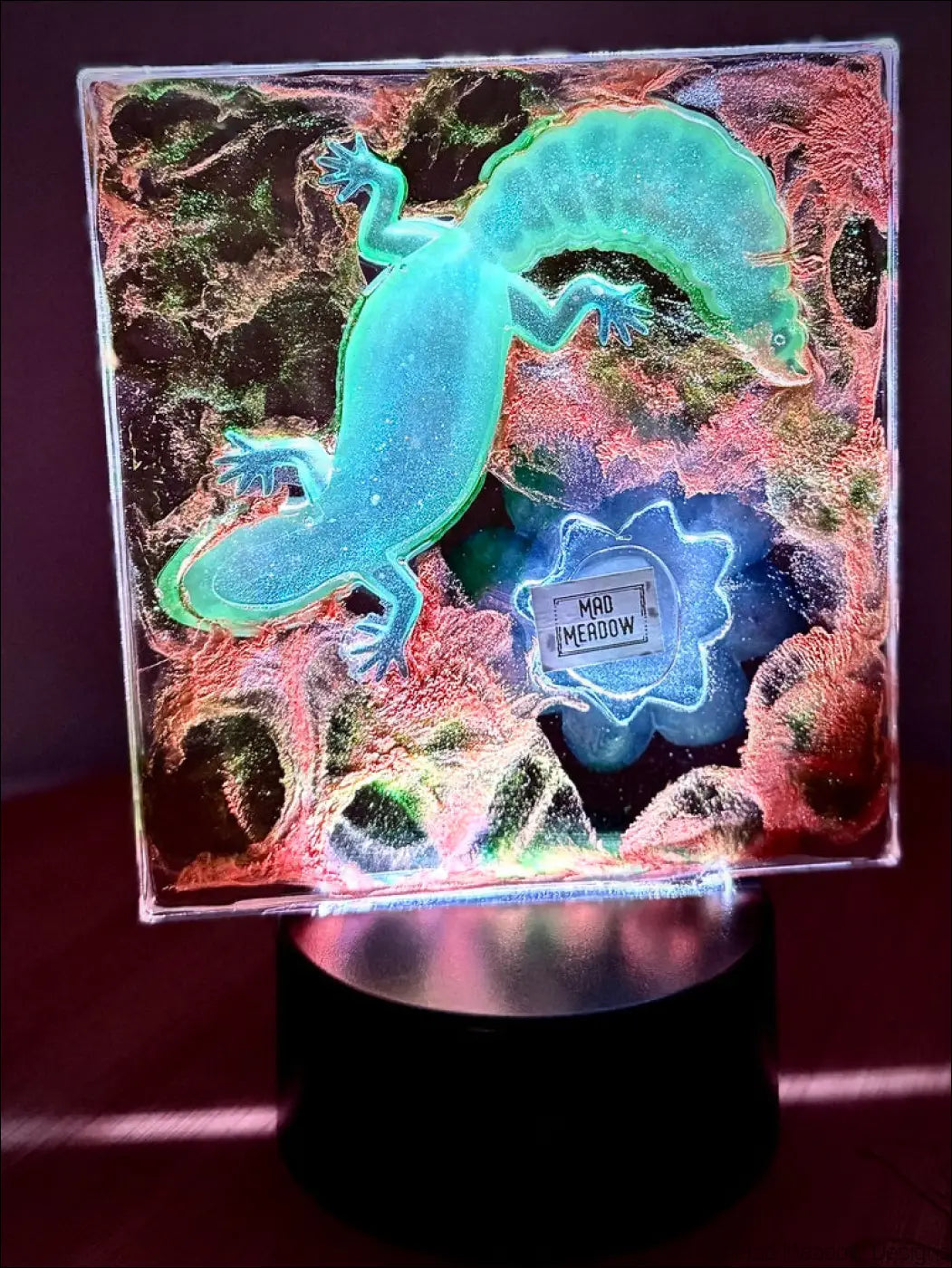 A glowing turquoise resin gecko with mad meadow label on a textured background water lily nightlight design