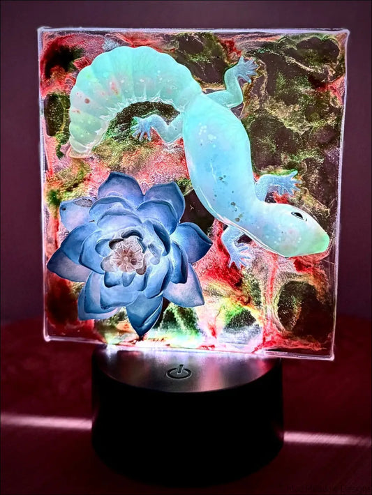 A glowing glass panel nightlight with a captivating blue gecko and layered blue water lily design