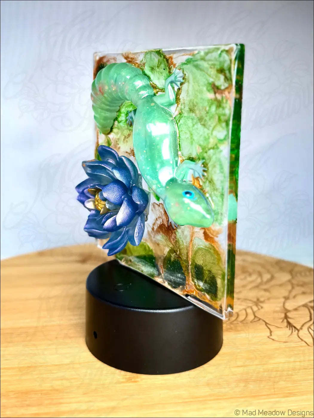 A translucent green captivating gecko figurine with blue eyes embedded in resin alongside a vibrant blue water lily nightlight